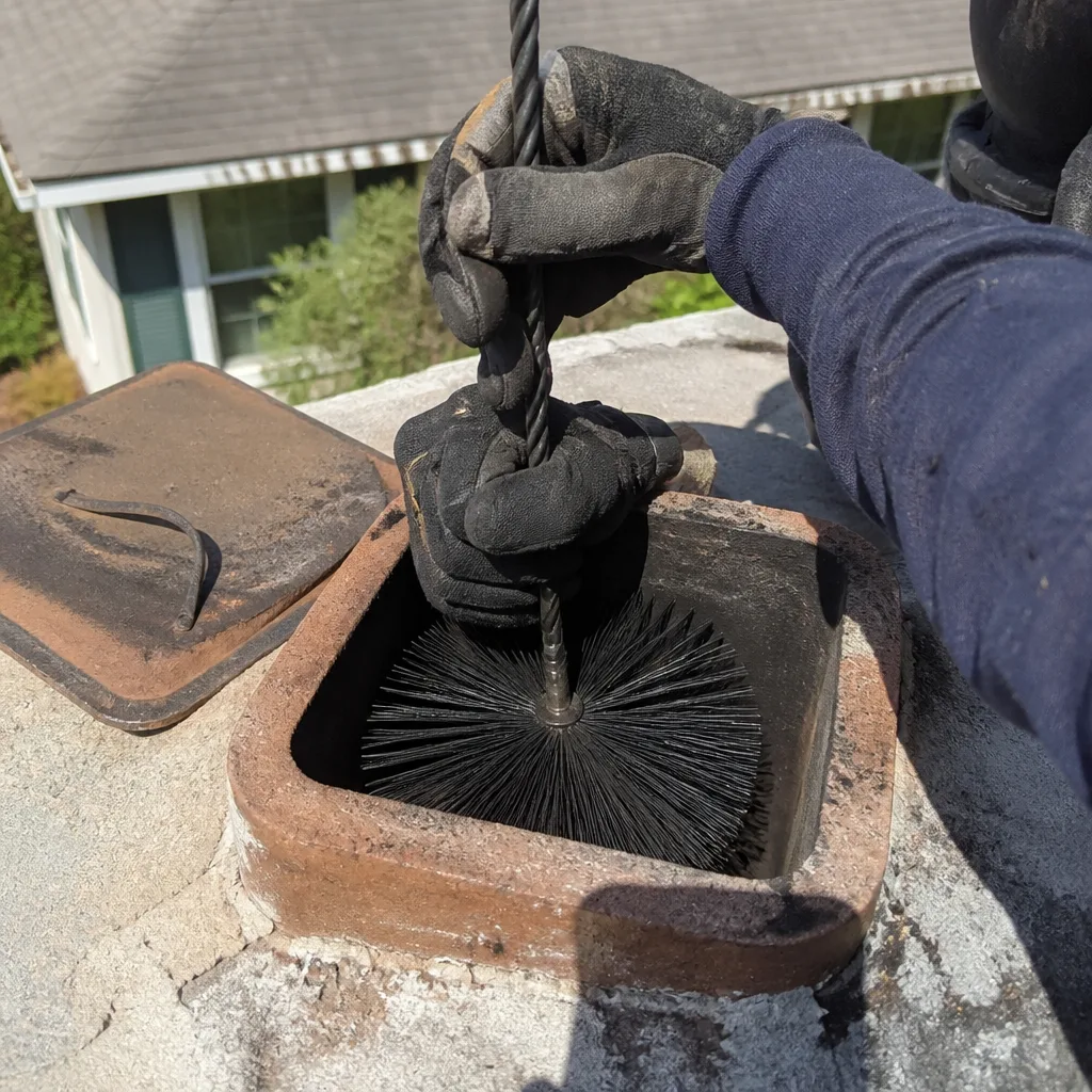 Professional chimney sweep cleaning a chimney flue with a wire brush